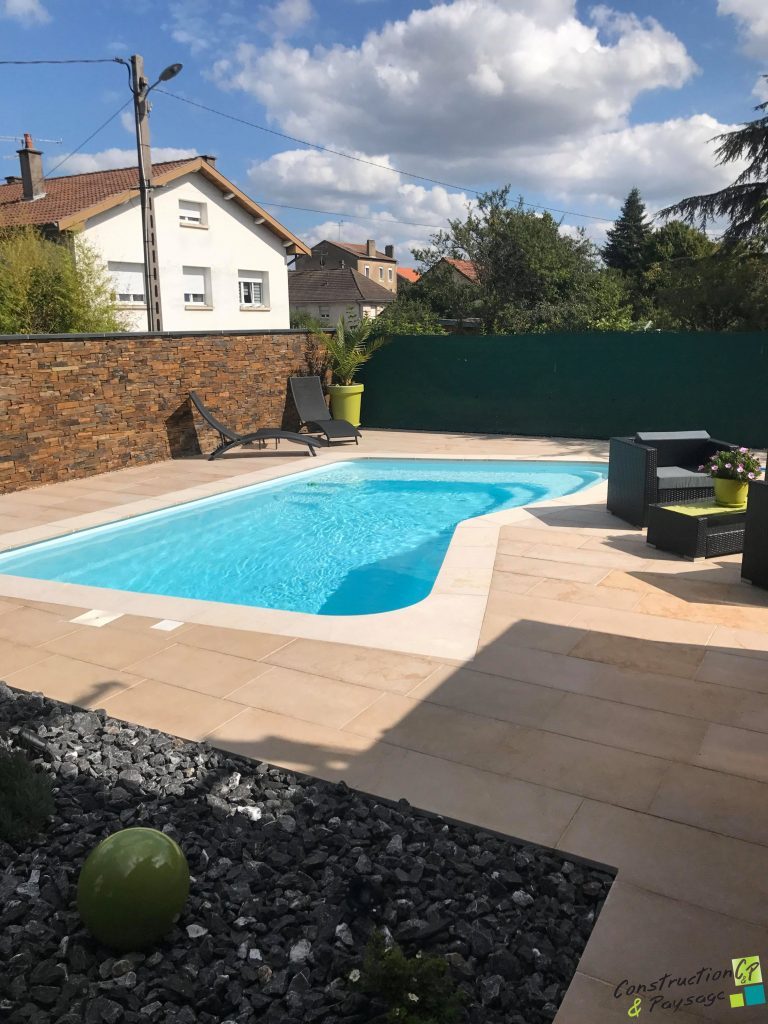 Piscine turquoise entourée de dalles beiges, mur en parement de pierre, transats et pots vert anis