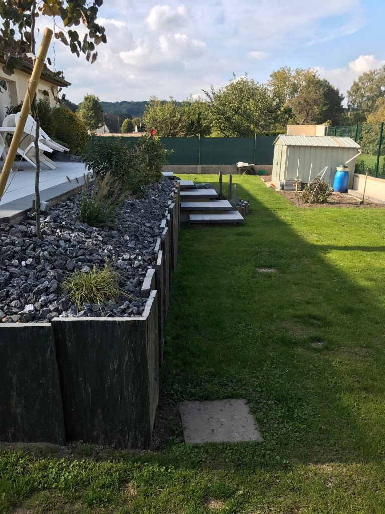 Le même jardin terminé : pelouse, bordure d'ardoises dressées, massif de galets et marches